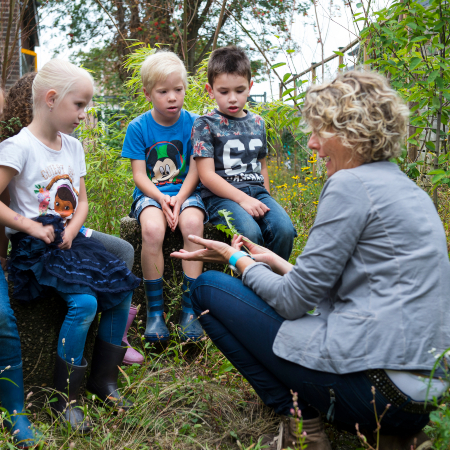 Op deze foto is een juf vier kinderen iets aan het leren over de natuur.